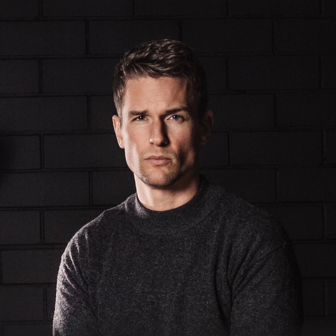 Flo Felter, founder and CEO of cosmos, in front of a dark brick wall.